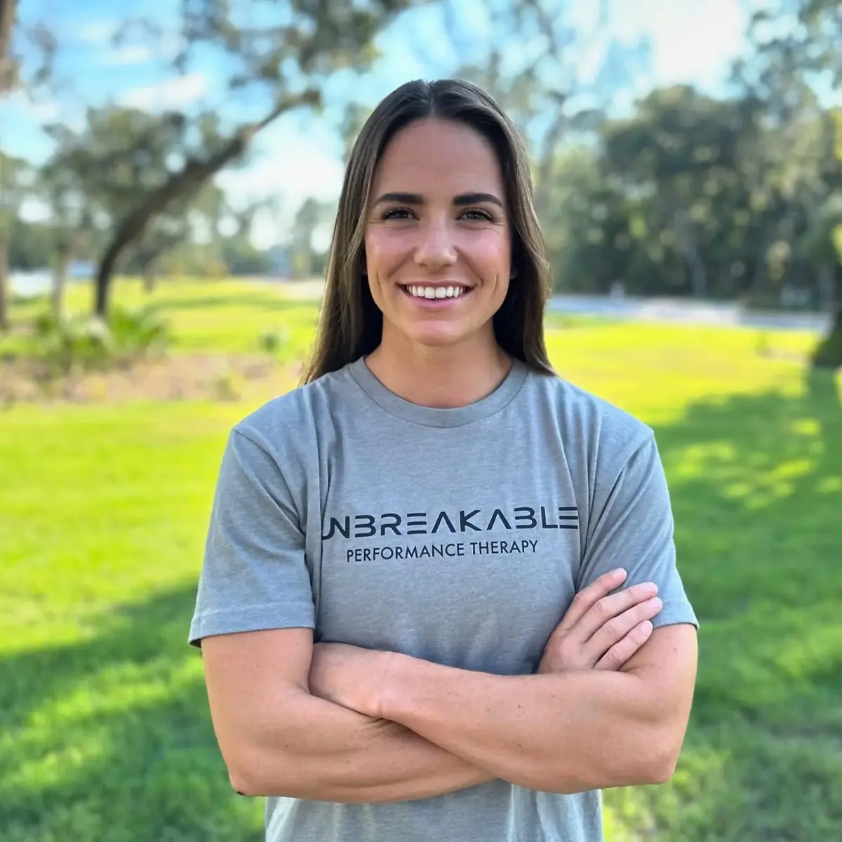 Emily smiling outdoors with her arms crossed