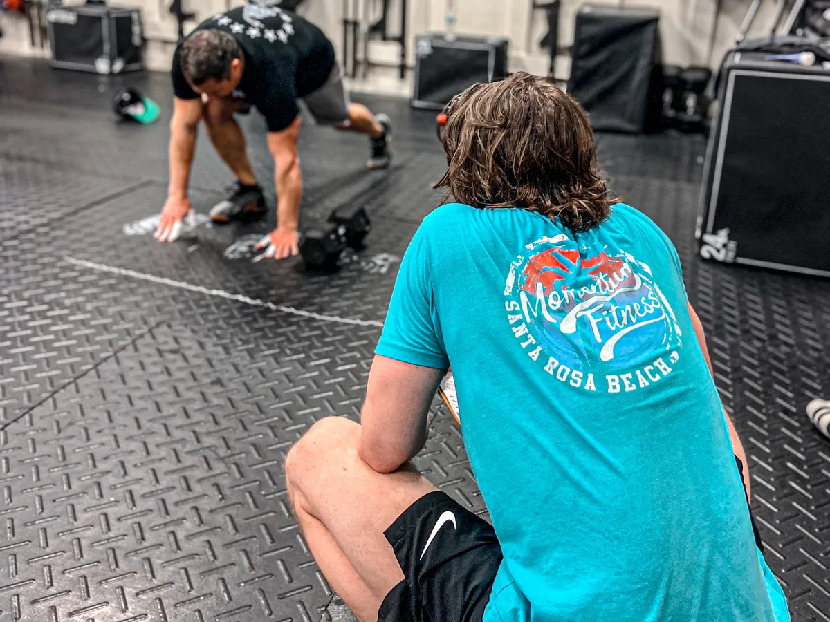 A coach in a Momentum Fitness shirt watching a member’s form