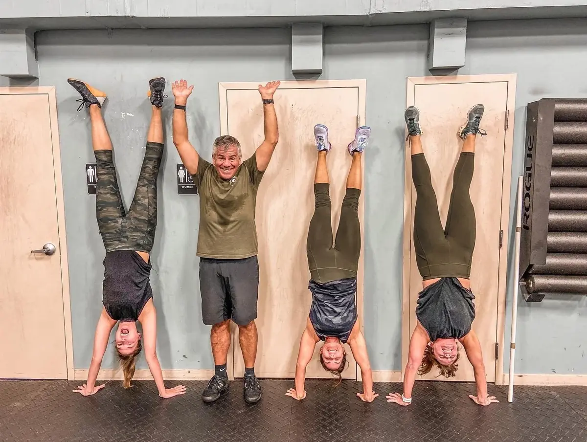 Members holding handstands against the wall with a coach standing between them