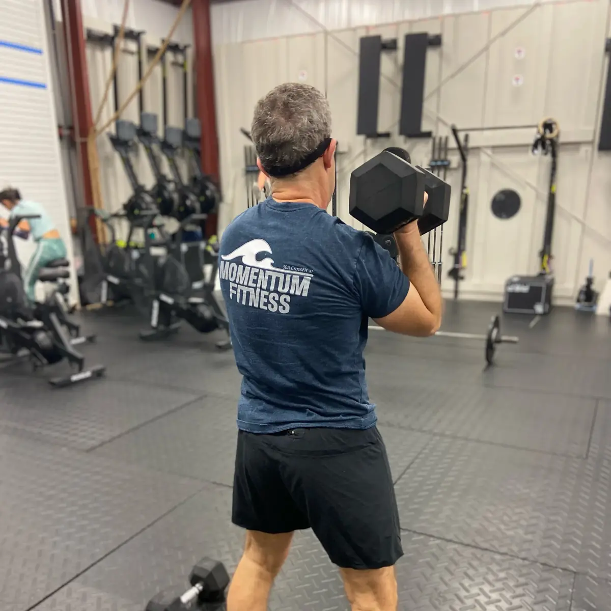 A member in a Momentum Fitness shirt carrying a dumbbell